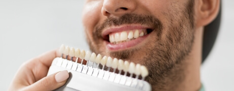 Dentist holding a tooth color chart next to a smiling patient