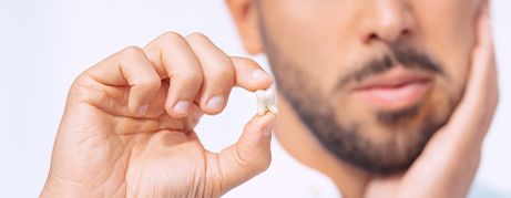 Man holding a tooth in one hand and holding his cheek in the other