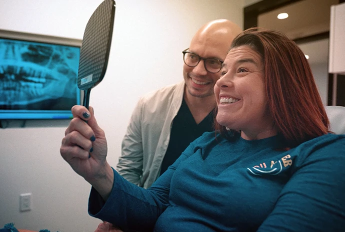 A patient admiring her new smile in a hand mirror with Dr. Silfa