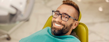 Man with glasses smiling while sitting in treatment chair