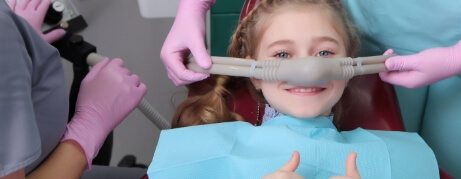 Young girl in dental chair giving thumbs up while receiving nitrous oxide