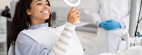 Woman smiling at reflection in handheld mirror